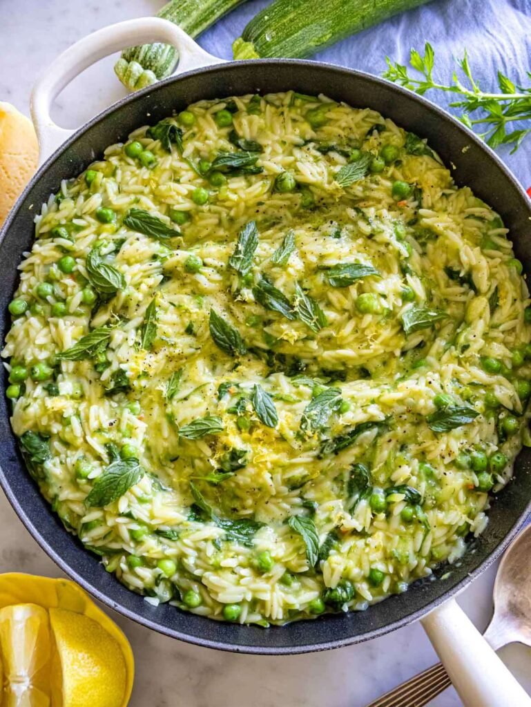 Overhead view of lemon orzo with zucchini peas and spinach in a white serving bowl